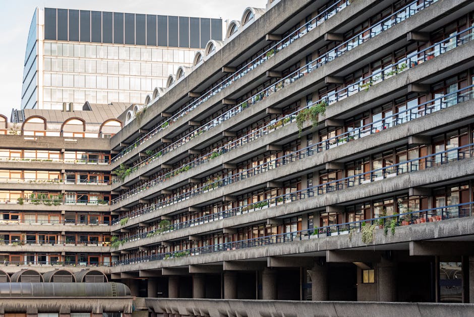 A multi-storey residential building with expansive balconies decorated with various potted plants, bushes, and small trees, creating a lush, green appearance against the grey concrete structure. The b