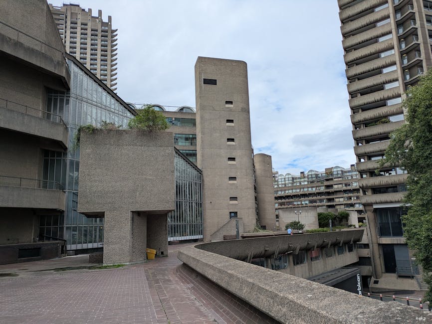 A close-up view of a modern urban residential building with multiple concrete balconies, some of which feature vibrant flower boxes filled with pink and purple petunias and green foliage. The balconie