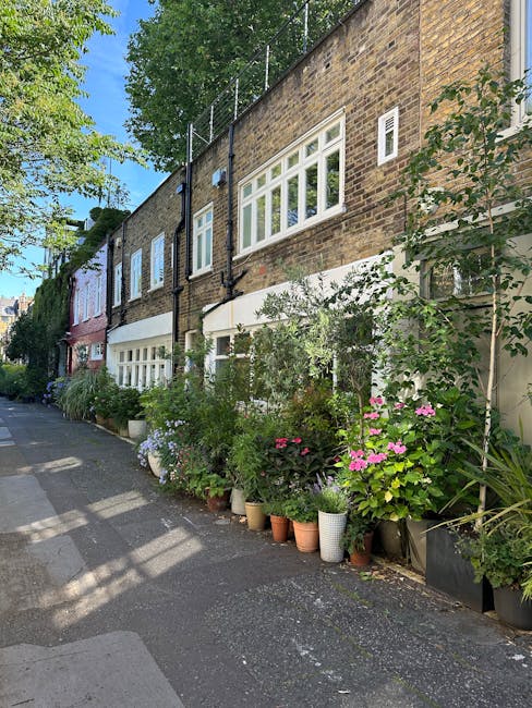 A row of brick terraced houses in an urban setting features a variety of potted plants and garden décor along the sidewalk. The buildings have traditional brick facades with window and door frames pai